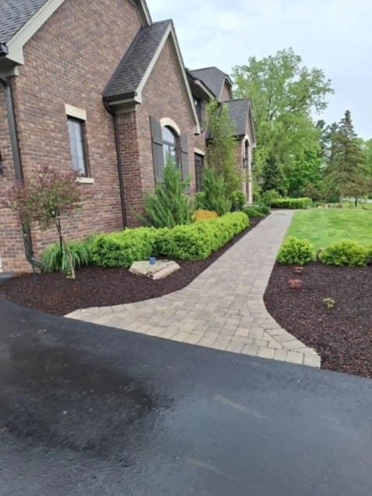 Brick estate home with curving paver walkway and lush foundation plantings