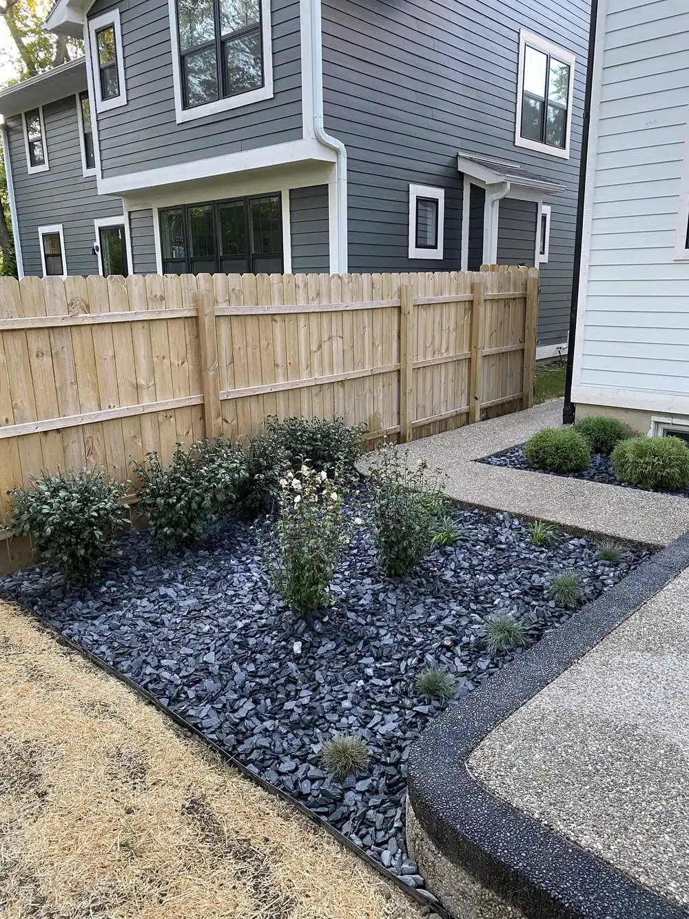 Finished side-yard landscape with dark decorative stone, shrubs, and a curved walkway
