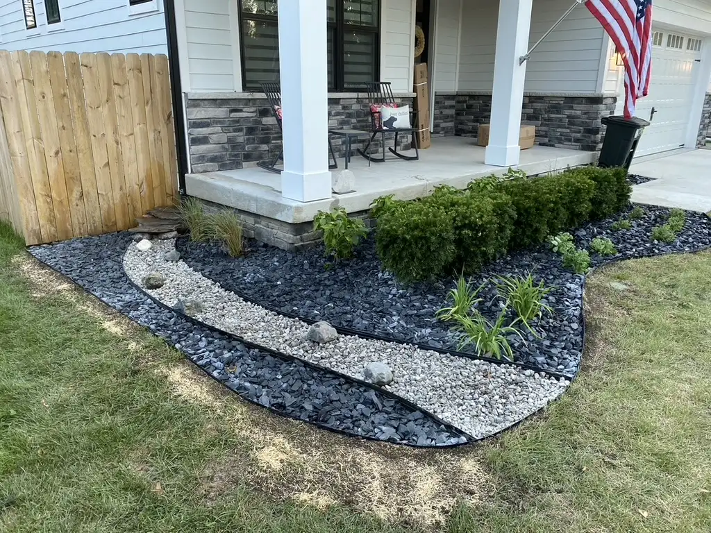 Finished front-yard planting bed with shrubs, stone, and curved edging