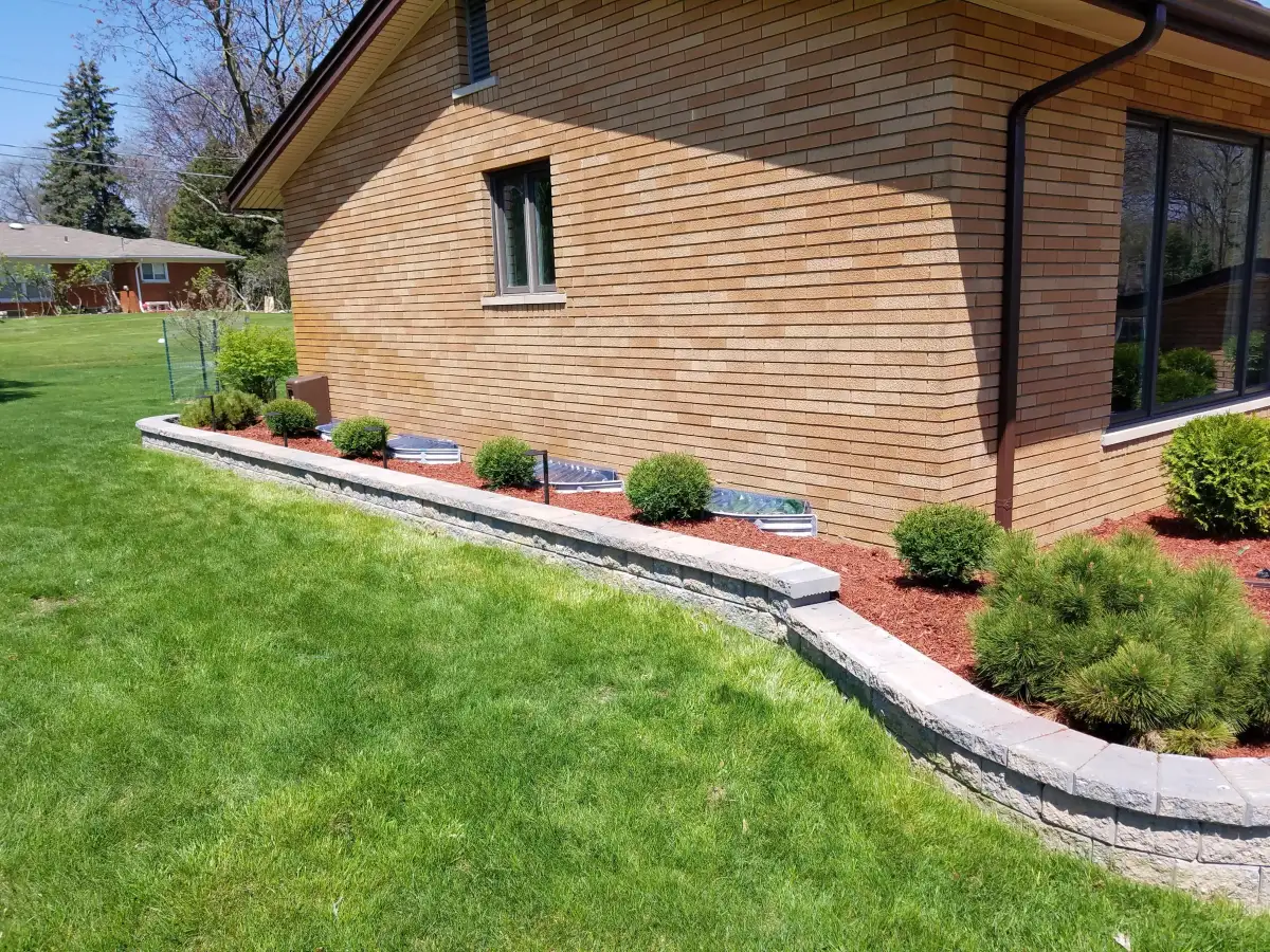 Finished retaining wall with capstones along brick home with shaped boxwood shrubs