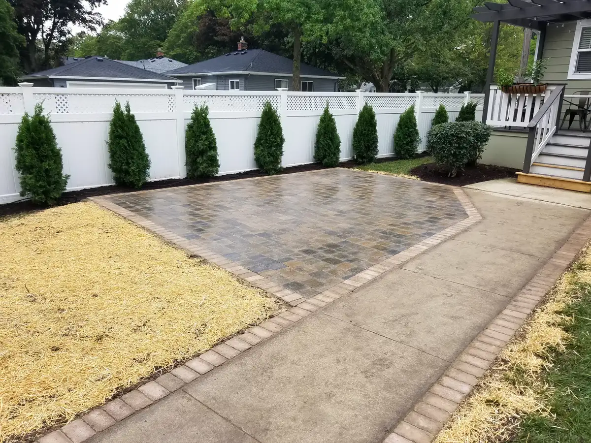 Completed paver patio with white fence and arborvitae border