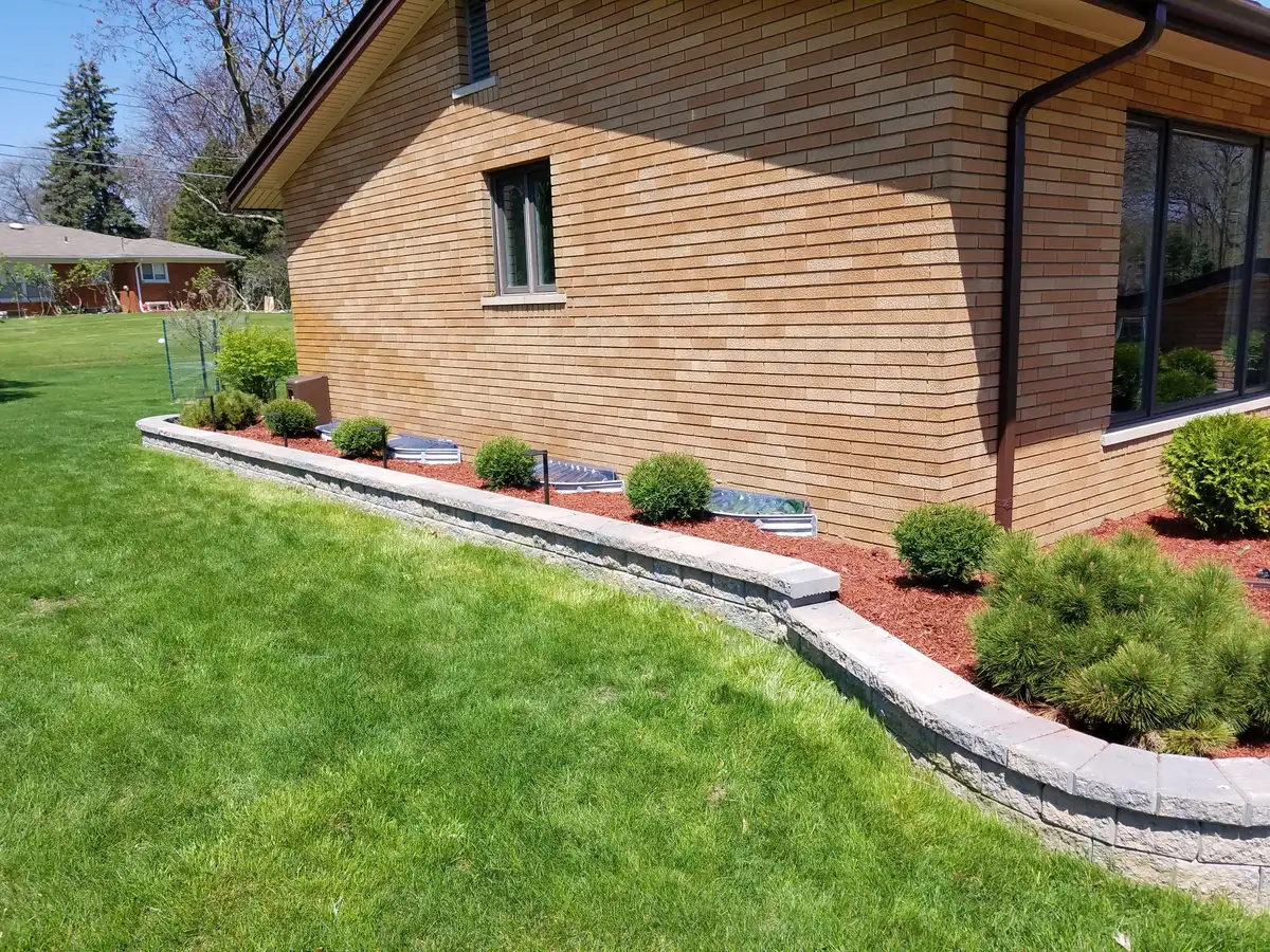 Low segmental block retaining wall with boxwood shrubs along brick home