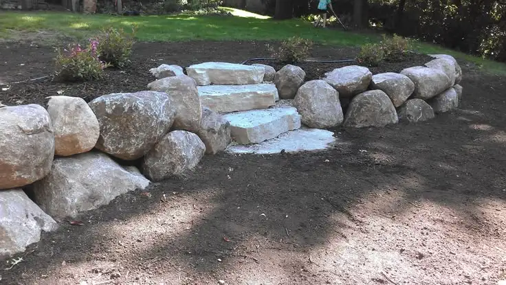 Large boulder retaining wall with natural stone slab steps in residential backyard
