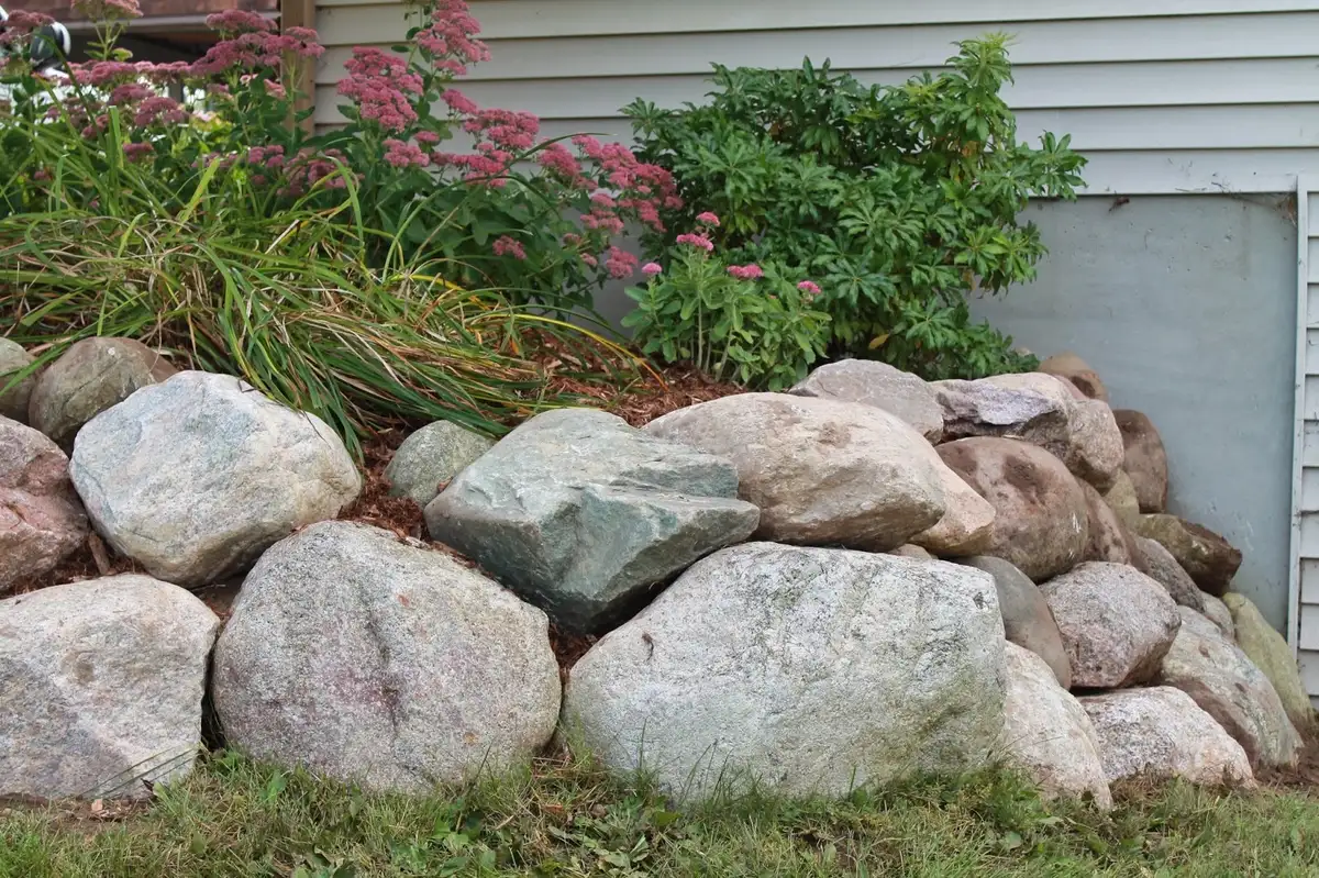 Natural fieldstone boulder retaining wall with flowering perennials along home foundation