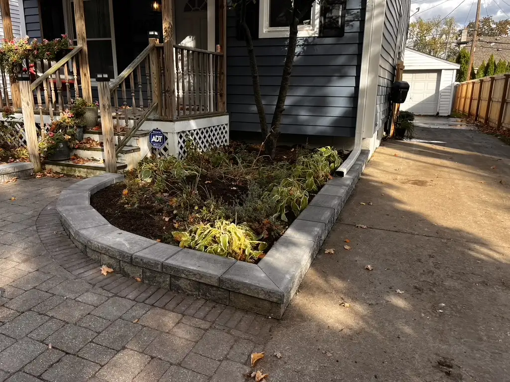 Curved block retaining wall planter with perennial plantings and paver walkway