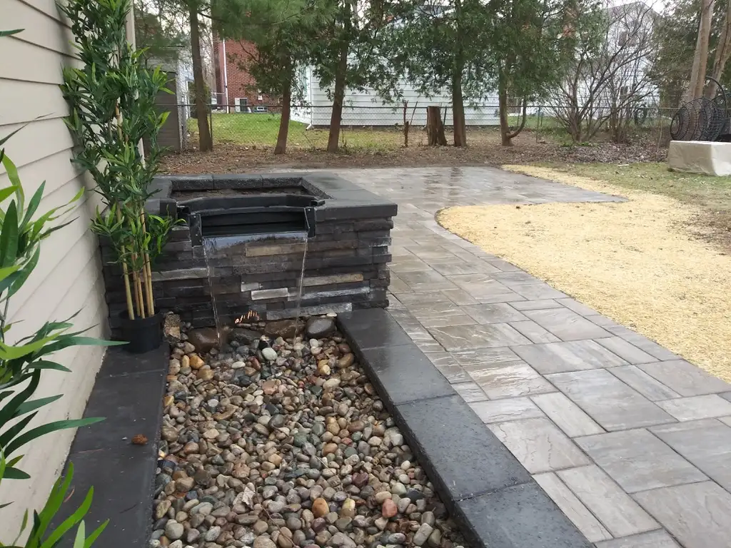 Raised stone water feature box with clean spillway design alongside paver patio