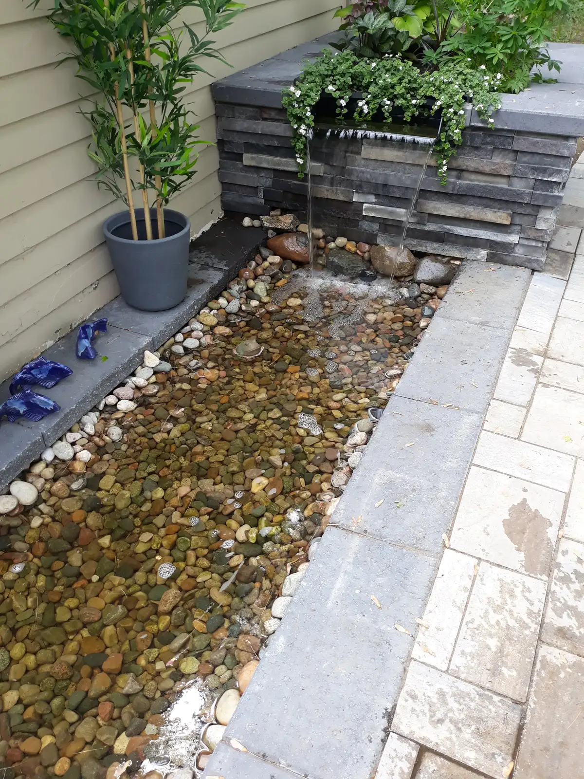 Rectangular stone water feature with spillway cascading into river rock channel