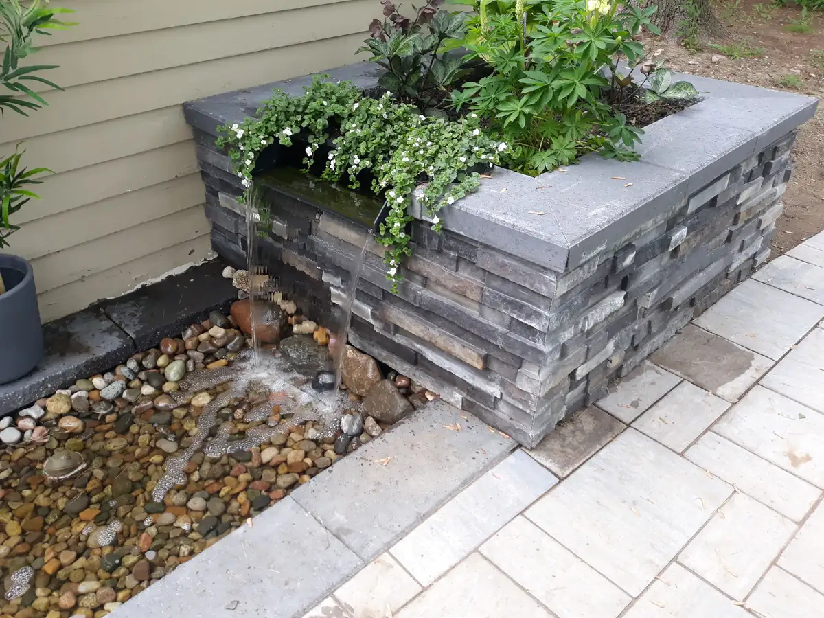 Raised stone pondless water feature with spillway cascading into pebble basin